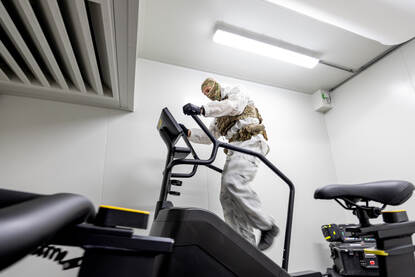 Een militair in wit pak loopt op een fitnessapparaat.