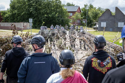Demonstranten, op de rug gezien, staan bij een met prikkeldraad afgezette brug oog in oog met de combat riot contol.