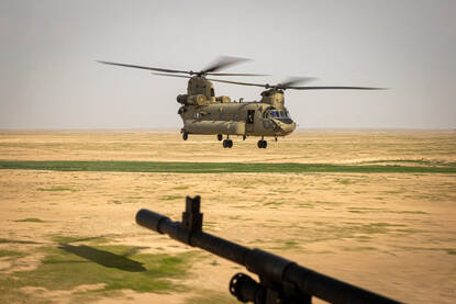 Een vliegende Chinook boven Irak met op de voorgrond een MAG-machinegeweer.