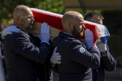 Militairen dragen een kist met daarover de Nederlandse vlag.