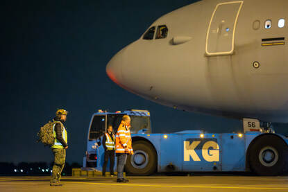 Neus van militair transportvliegtuig in beeld met militair en grondmedewerker ervoor.