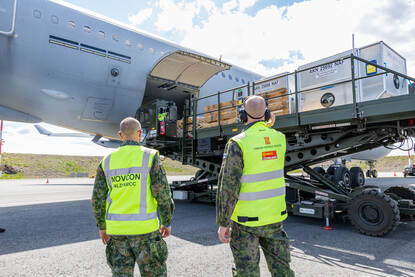 Twee militairen in gele hesjes zien toe hoe vracht het vliegtuig wordt ingeladen.