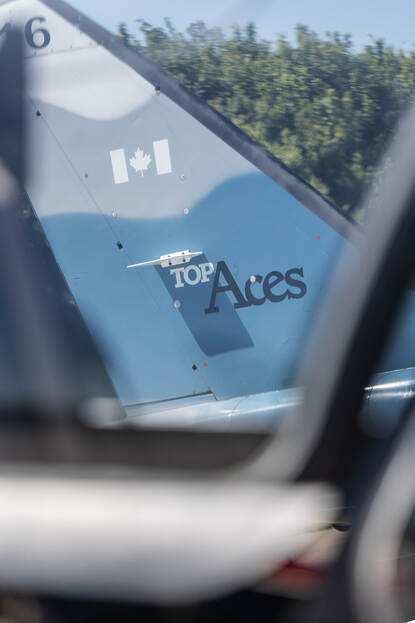 De blauw-grijs gecamoufleerde staart van een Alpha Jet met daarop het Top Aces-logo, gezien door de cockpit van een ander vliegtuig.