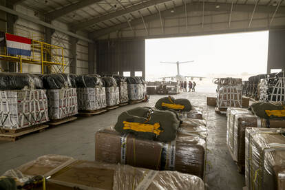 Links een foto van een ingepakte parachute op een bundel. Rechts een rij bundels in een hangar met een Duitse A400M op de achtergrond.
