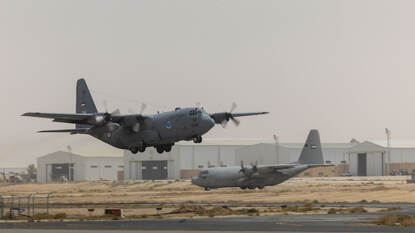 En Jordaanse C-130 stijgt op terwijl een C-130 van de Verenigde Arabische Emiraten naar de startbaan taxiet.