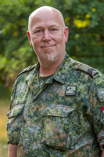 Portretfoto van sergeant Hans, achter hem bomen.