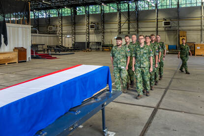 De ploeg loopt strak in de pas richting de kist. Daarna tillen ze deze op de schouders.