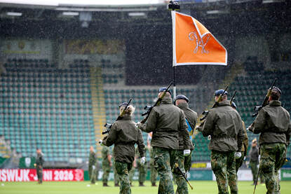 De vaandelwacht van de luchtmacht betreedt het veld vanuit een hoek van het stadion. De vaandeldrager in het midden, daaromheen militairen die een Colt C8-geweer vasthouden.