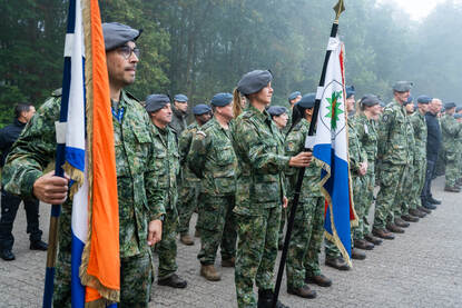 Militairen op een rij waarvan een aantal een vlag vasthouden.