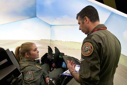 Prinses Amalia krijgt uitleg van een vlieger terwijl ze in de cockpit van een flightsimulator zit.