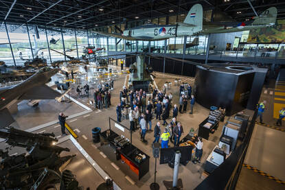 Overzicht in het Nationaal Militair Museum met veel bezoekers en een Chinook-transporthelikopter op de grond en diverse helikopters en vliegtuigen hangend aan het plafond.