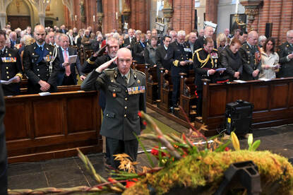 Brigadegeneraal Dick van Broekhoven brengt een groet aan de krans. Op de achtergrond kerkbanken met militairen en burgers.