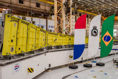 Een stalen gelen balk en aan de zijkant vlaggen van Nederland, Vliegbasis Eindhoven en Brazilië.