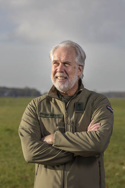 ‘Een militair in een groene jas staat met armen over elkaar en kijkt lachend in de camera.