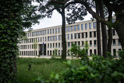 Een doorkijkje via de bomen naar het nieuwe, zandkleurige kantoorcomplex van het LTC.