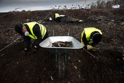 Twee forensisch onderzoekers zitten op hun knieën en zoeken sporen op crashsite MH17.