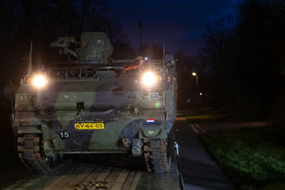 Voorzijde YPR-765 met lampen aan in schemerdonker.