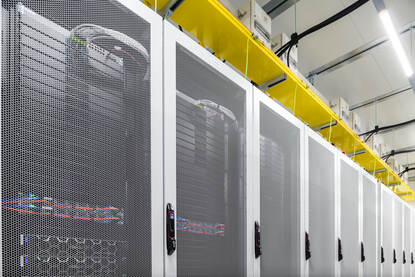 Rij serverkasten met gaasdeuren en daarboven gele kabelgoten.