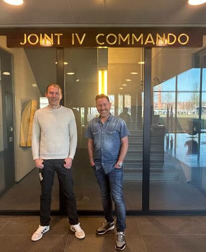 Twee mannen staan naast elkaar voor de ingang van hun werkplek.