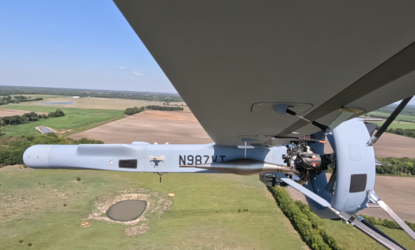 De grijze V-BAT vliegend door de lucht. Vastgelegd vanonder een van de vleugels. Op de zijkant staat een serienummer in zwarte cijfers.