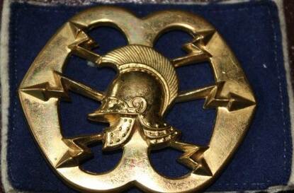 het embleem van de verbindingsdienst met daarop een geniehelm geflankeerd door 6 bliksemschichten.