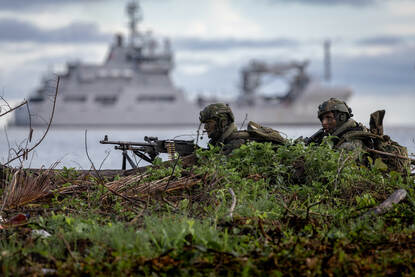 Links een Frisc-onderscheppingsvaartuig met Pelikaan op de achtergrond. Rechts mariniers in dekking met de Pelikaan op de achtergrond.