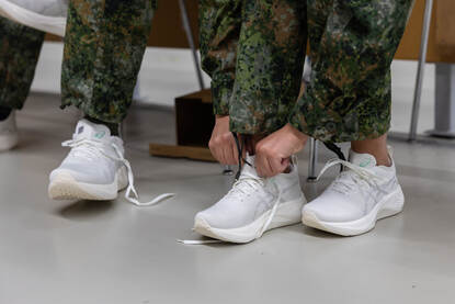 Links twee witten sportschoenen op een tafel, rechts twee militairen trekken de schoen aan.